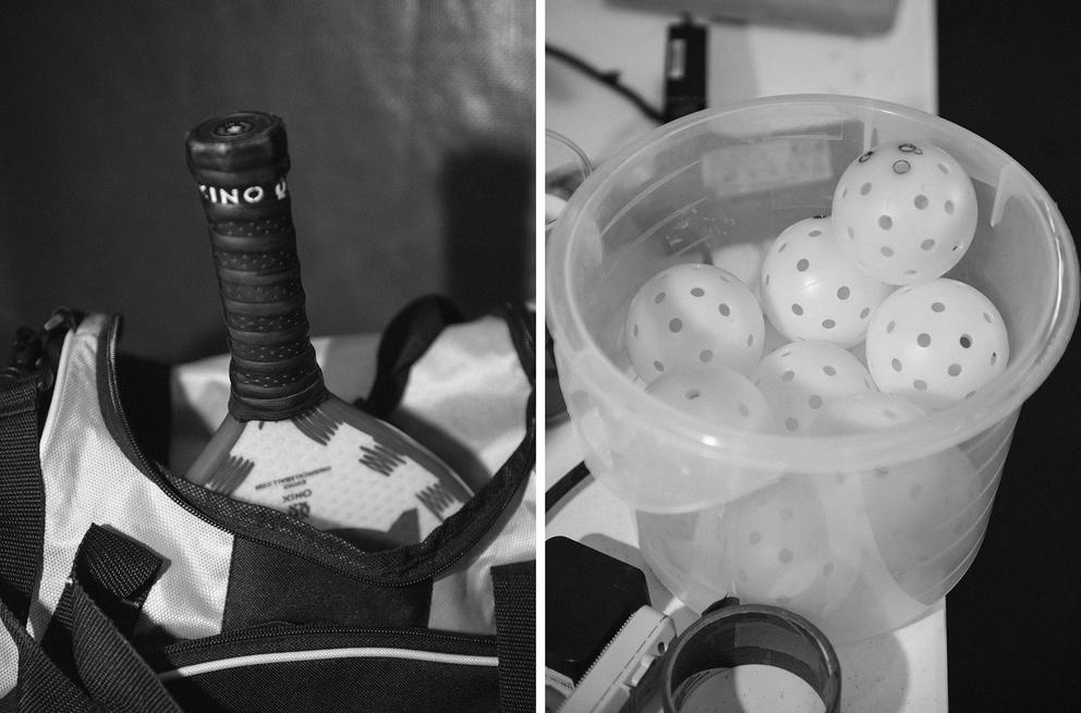 A pickle ball racket and bucket holding pickleballs. Black and white.