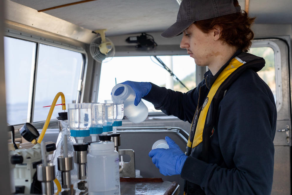 A man pours water samples over testing equipment inside a boat