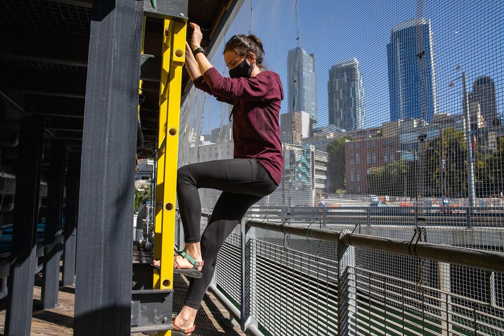 A woman climbs down a ladder with the Seattle skyline behind her