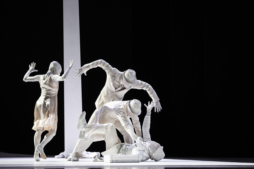 photo of a dance performance on stage where dancers in all white appear to struggle with each other