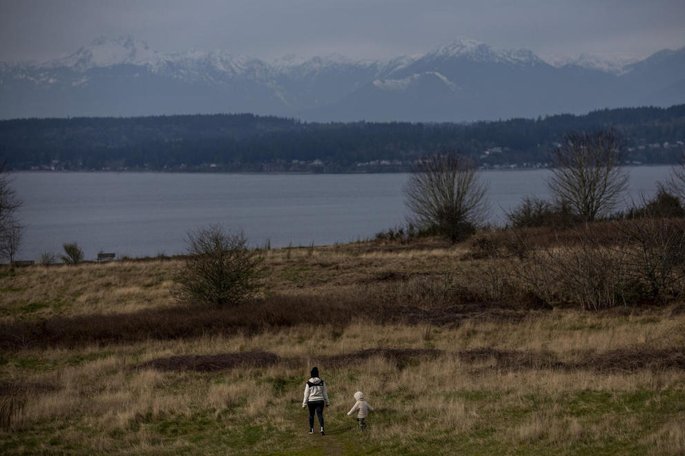 two figures stand on a trail in Discover Park looking out toward the Puget Sound