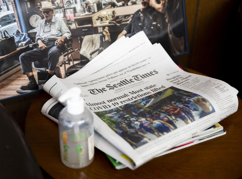A copy of the Seattle Times newspaper rests on a table next to a bottle of hand sanitizer. The headline read "Almost normal: Most state COVID-19 restrictions lifted"