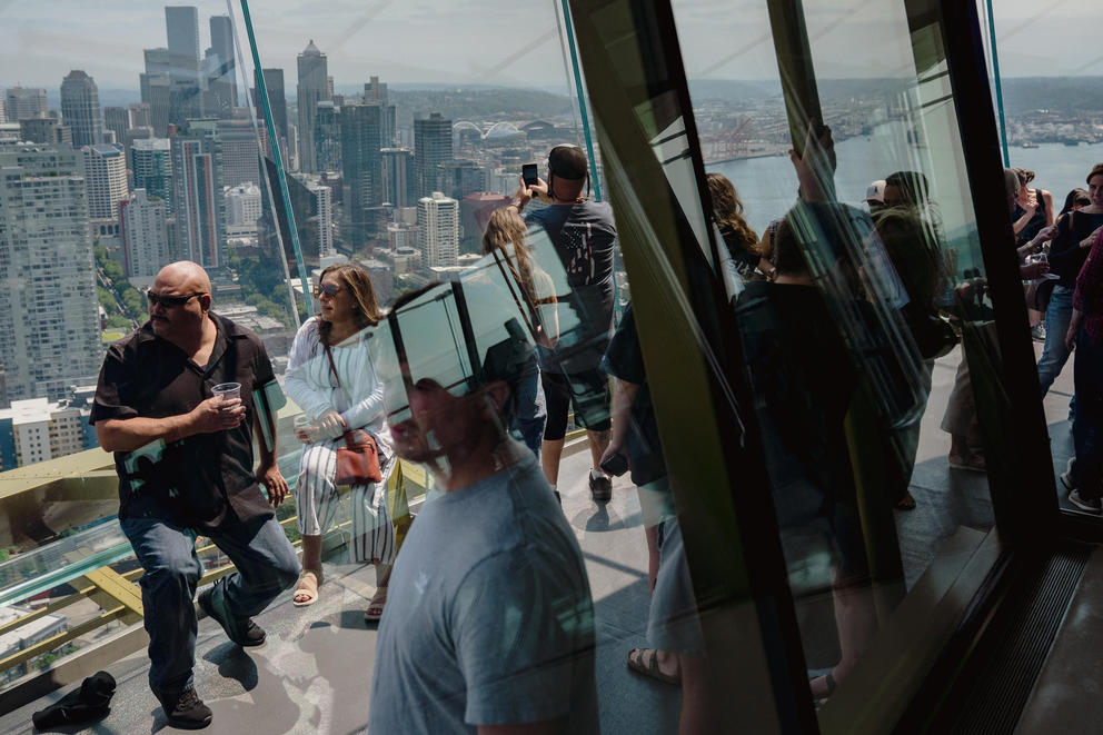 A crowd of people gather looking out at the Seattle skyline from the viewing deck of the Space Needle