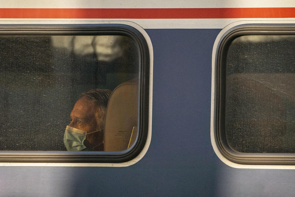 A masked passenger is lit by the evening sun, as he looks out the window of an Amtrak train at King Street Station