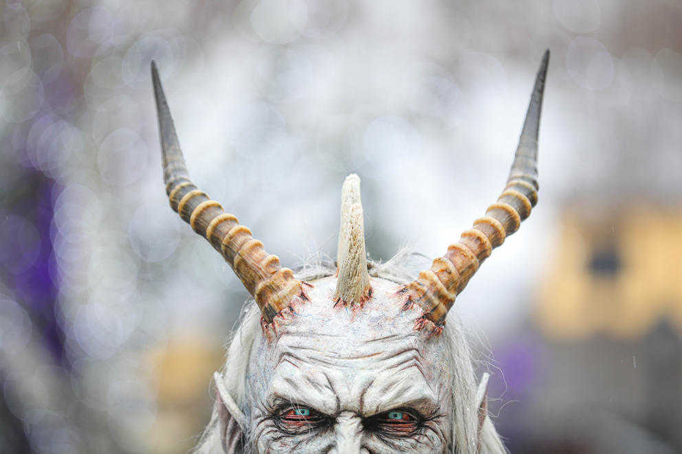 The eyes, forehead and horns of a demon-like Krampus mask are visible, the background fades out of focus