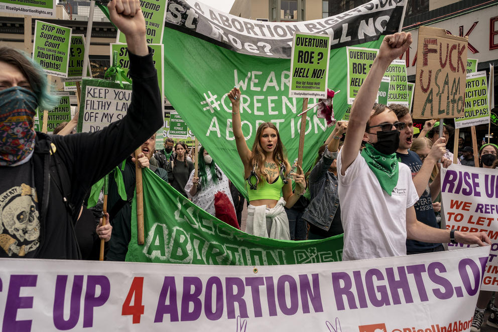 A group of people marches with their fists up, wearing green and holding a green banner