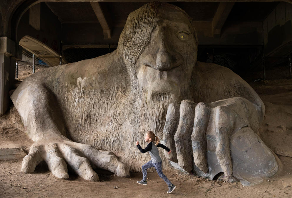 A child runs in front of a looming stone troll sculpture