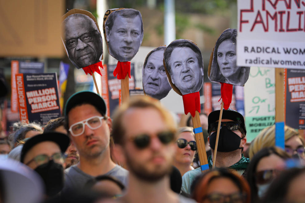Cutouts of the faces of five conservative Supreme Court justices are held above the crowd as thousands gather