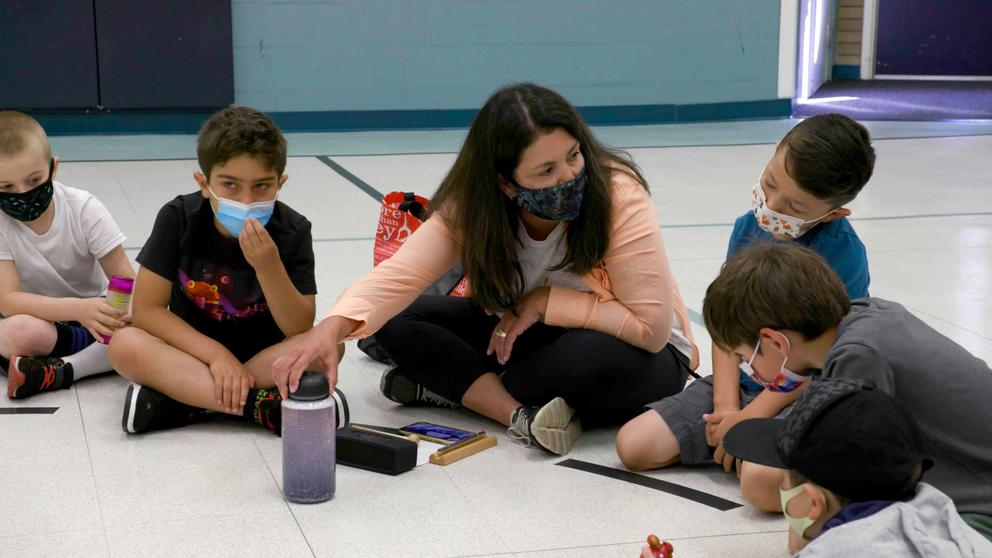 A teacher sits on the floor with some young students