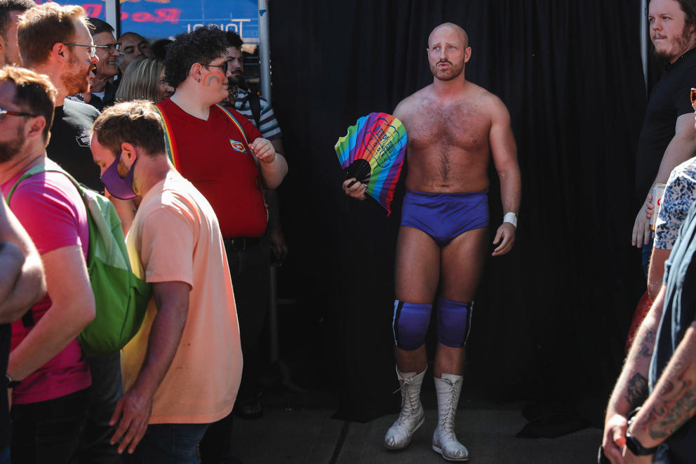 a man wearing purple wrestling garb and holding a rainbow flag 