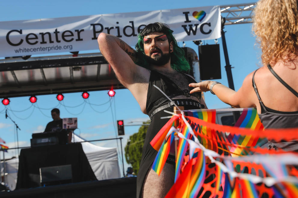 a drag queen preforms in front of a stage and banner reading Center Pride