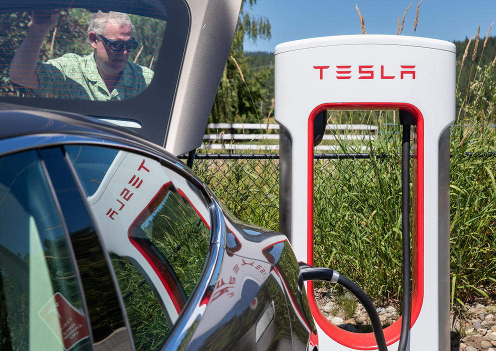A man is seen through his car window as he charges the vehicle at a Tesla charging station.