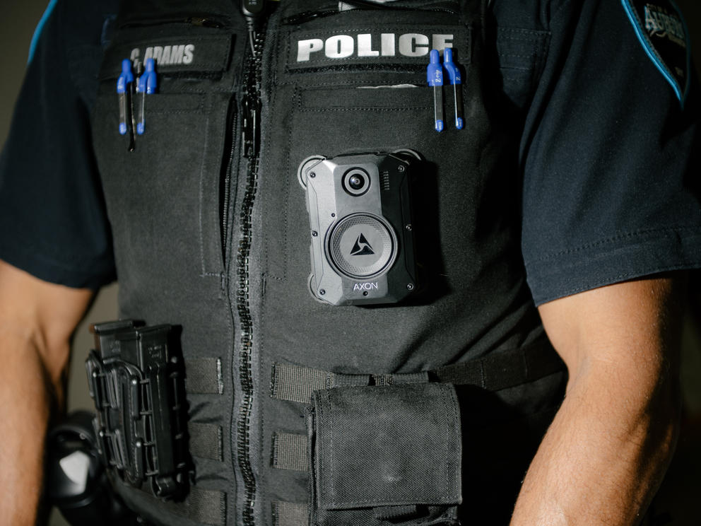 A small body camera is shown mounted to the chest of a uniformed police officer.