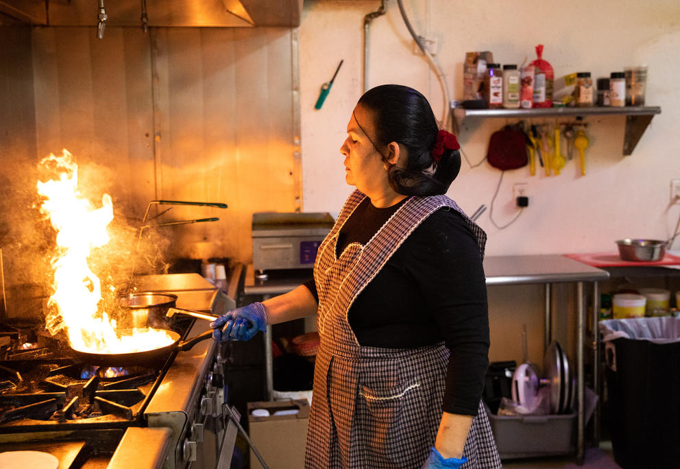 Flames rise from a frying pan as a woman cooks Mexican food on a stove. 