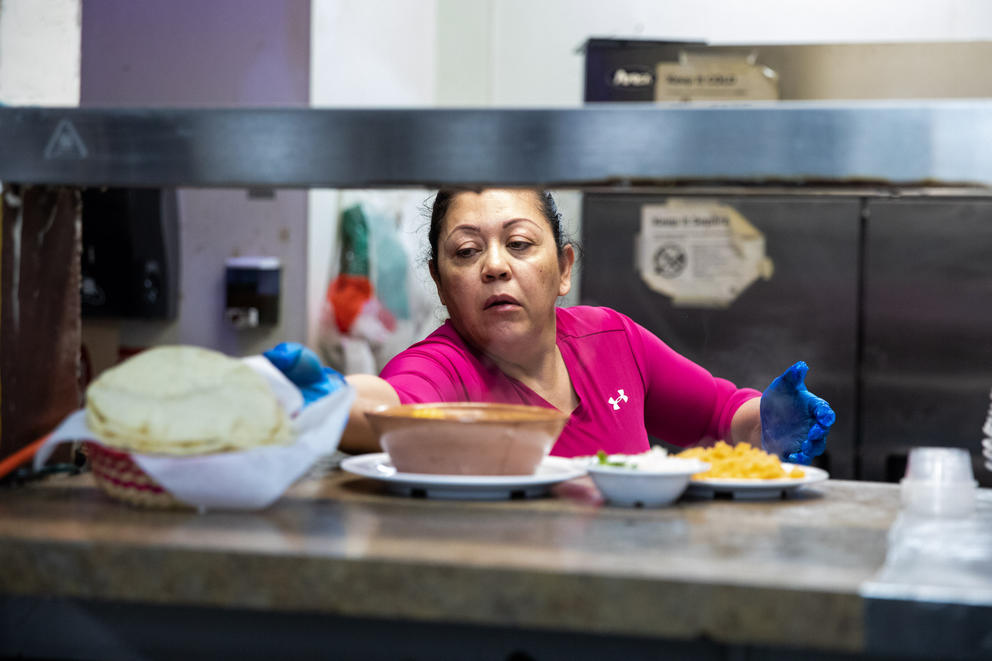 Maria Mendoza places a plate of food into a stainless steel order window.