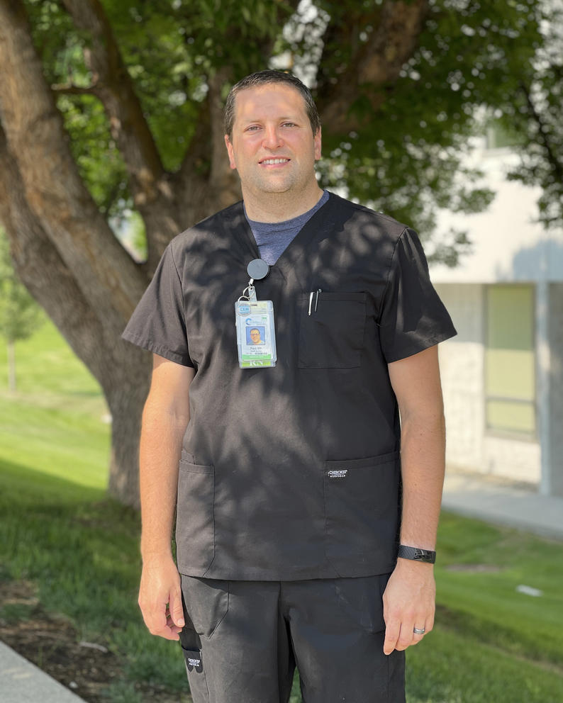Paul Fuller stands for a portrait outside under a tree in his nursing scrubs