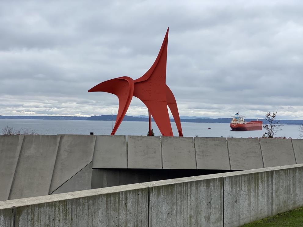 a large red abstract outdoor sculpture against a cloudy sky