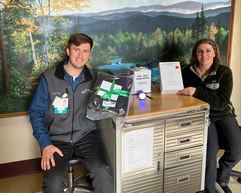 Two nurses pose with exam cart and gear 