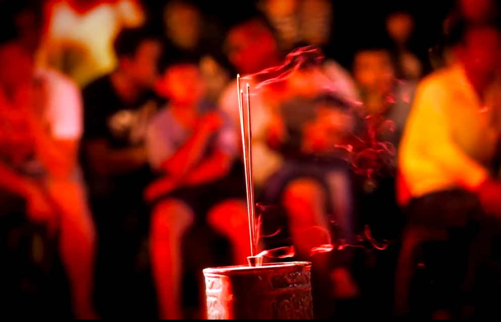 Smoldering incense in front of crowd basking in orange and red light