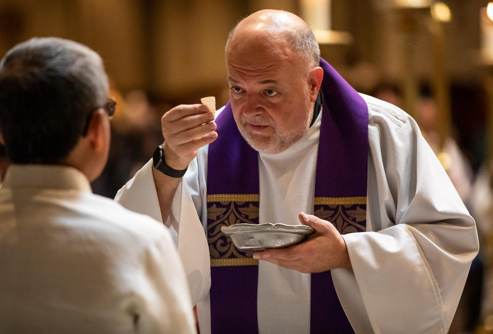 A close up of a priest holding up a wafer before a parishioner during mass