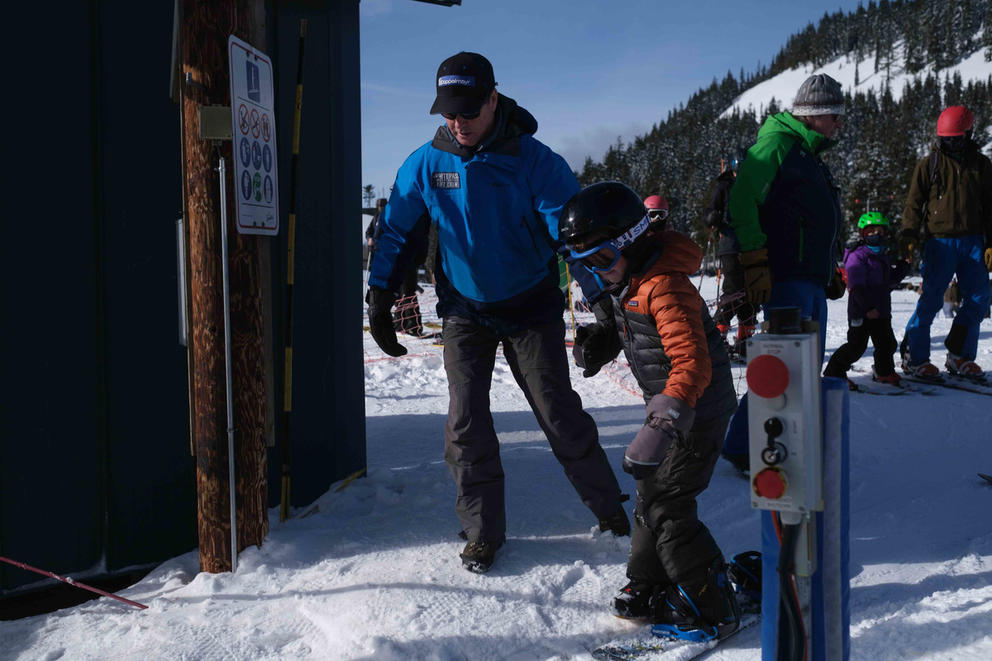 Ski area manager helping snowboarder on tube lift 