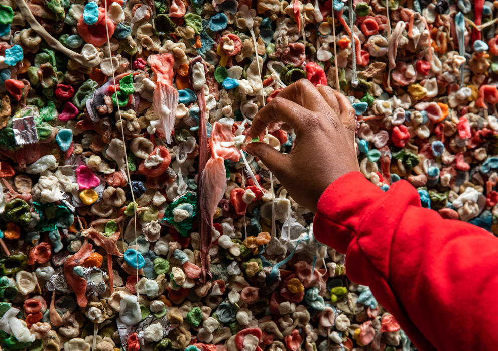 a hand puts gum on a wall of gum
