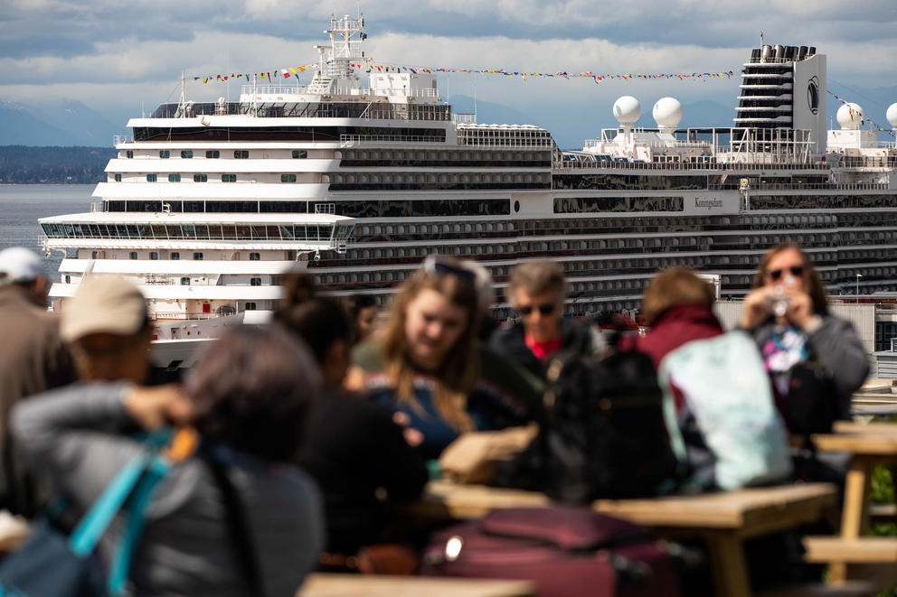 A giant cruise ship rises up behind people sitting at outdoor tables