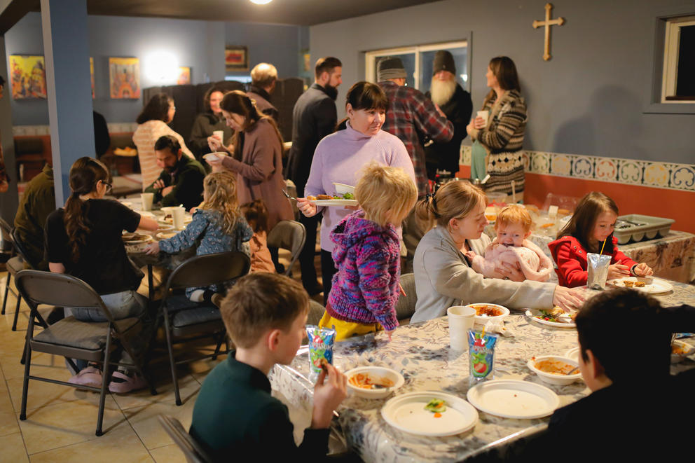 A group of people, including several children, walk around and sit at tables eating food.