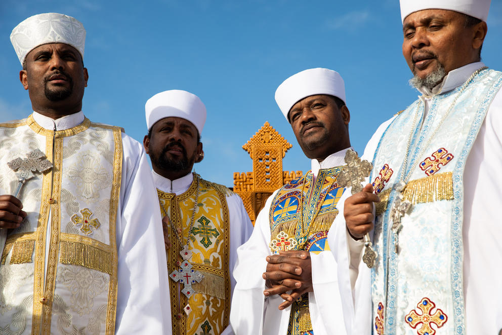 A group of Ethiopian orthodox priests in gold and white traditional robes are seen from below