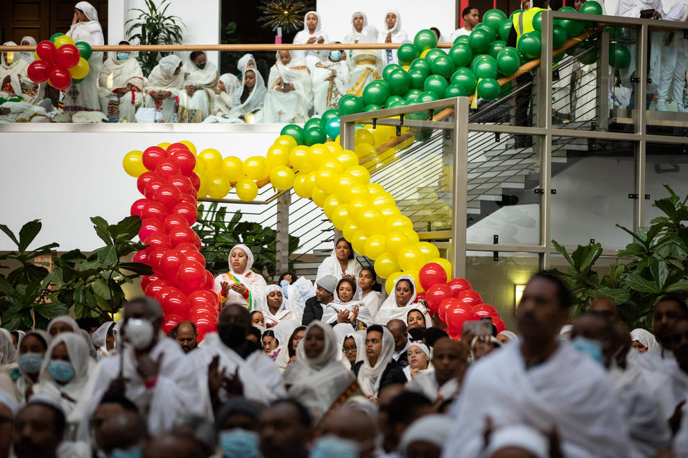 Parishioners in white gather around a stairwell lined with green, red and yellow baloons