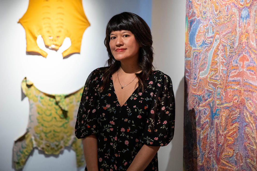 A woman in a floral dress smiles in front of colorful, abstract artwork hung on the walls