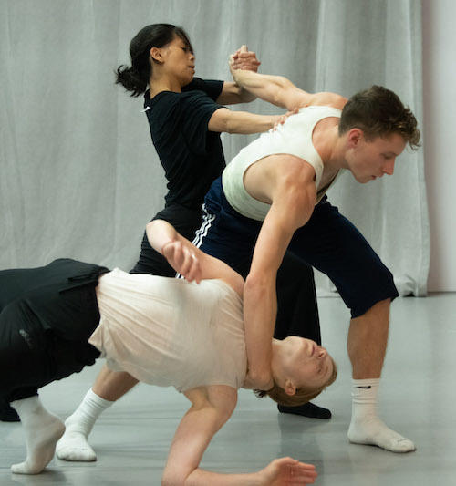 three modern dancers wearing black and white grip each other in a tangle