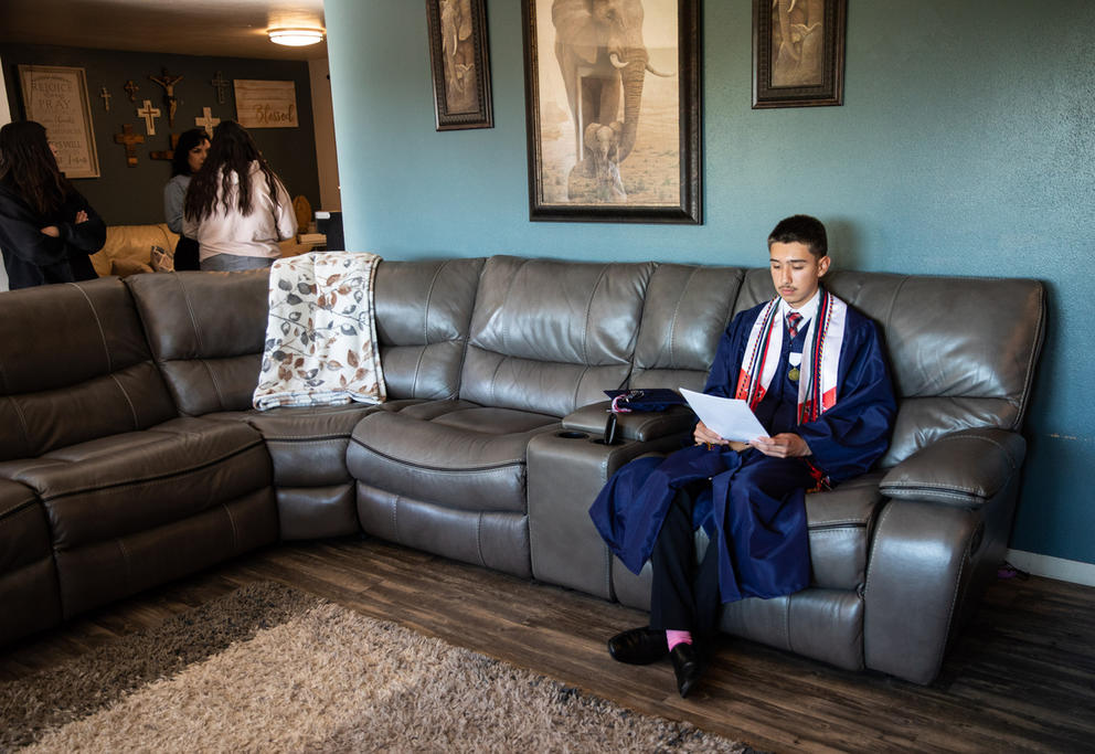 Man in cap and gown sitting on a couch reading