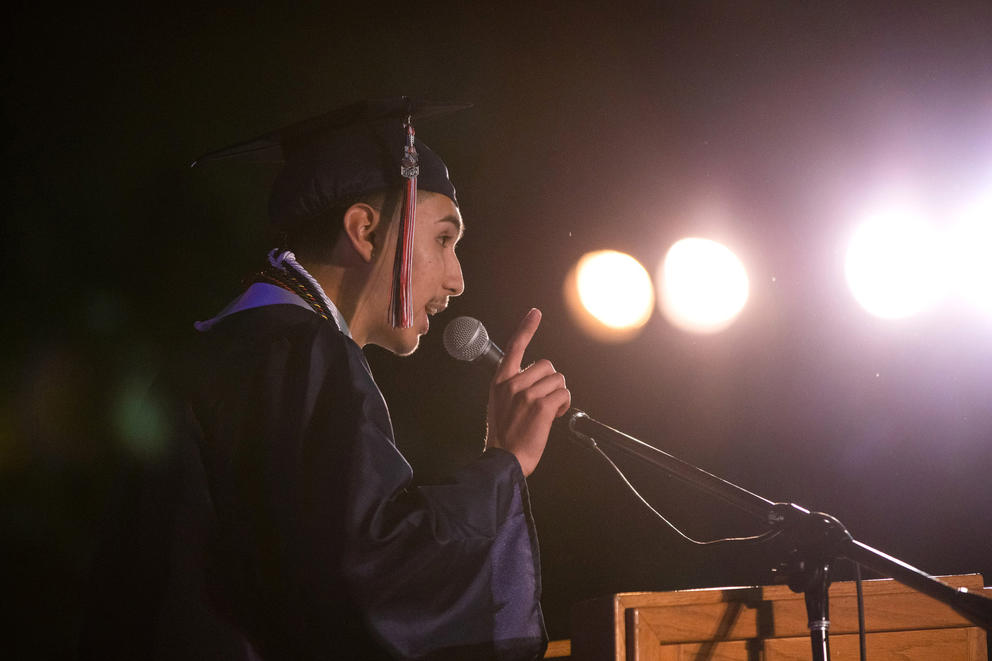 Man in cap and gown speaking into a microphone