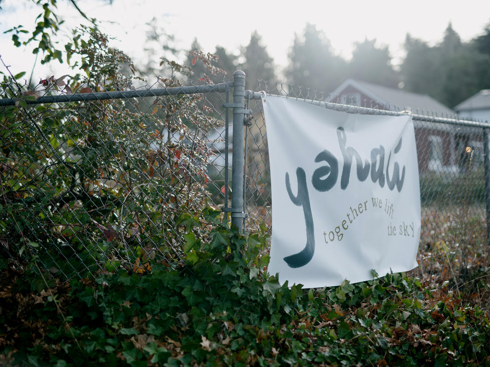 A fence features a white sign that says yəhaw̓ in black letters