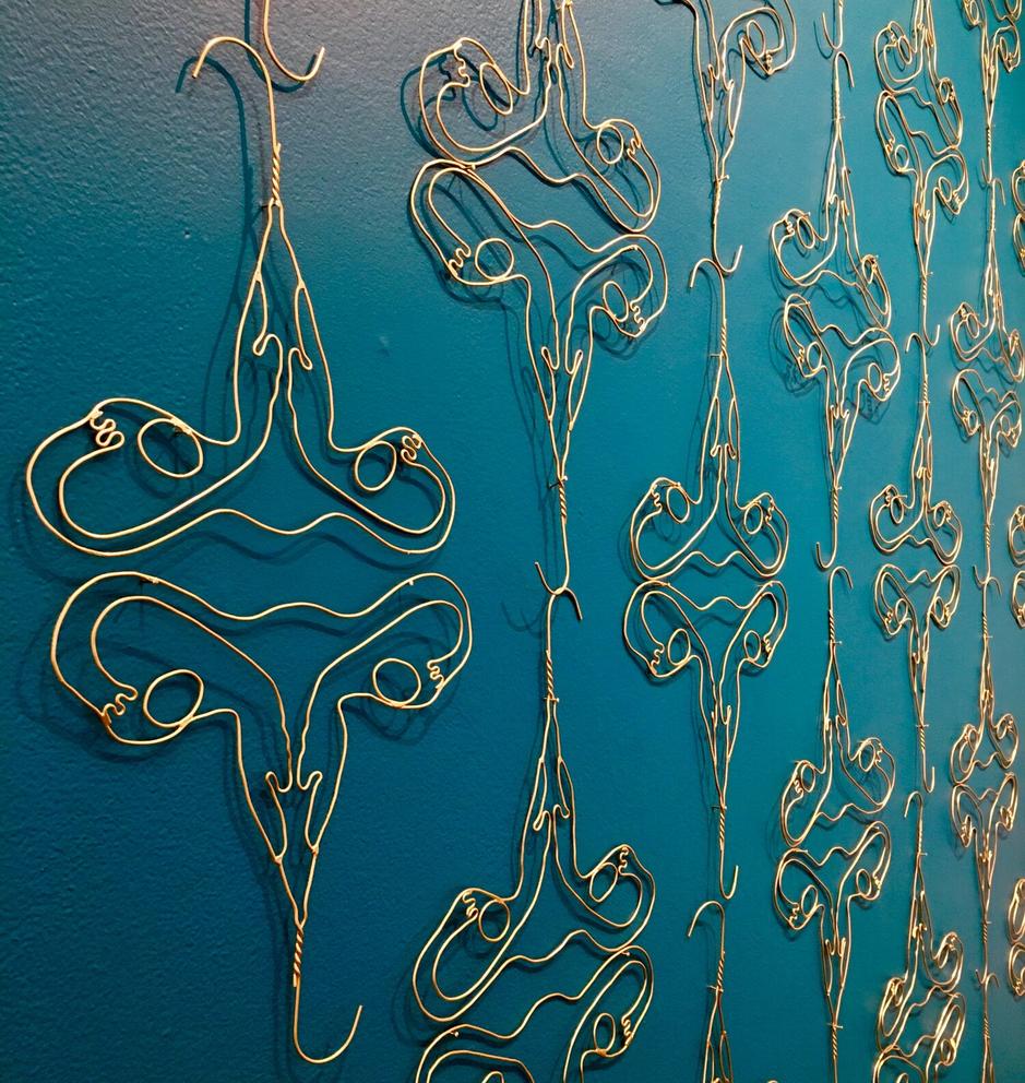 Gold hangers contorted into female reproductive systems against a teal blue wall