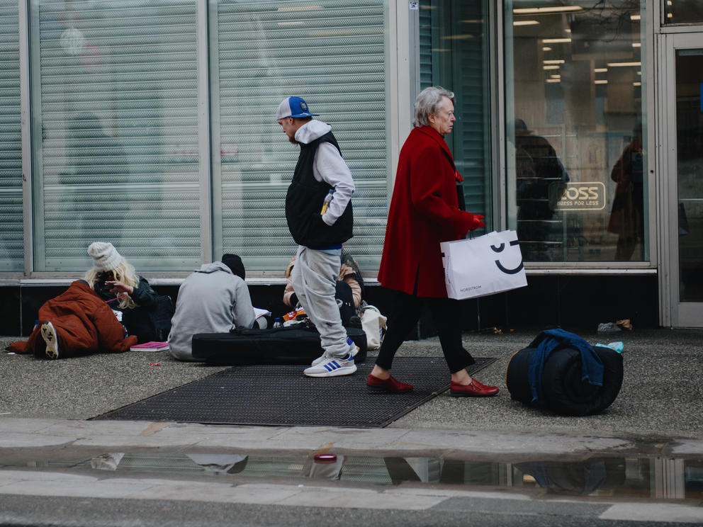 Pedestrians walk by three homeless people sitting on the ground on third avenue in seattle