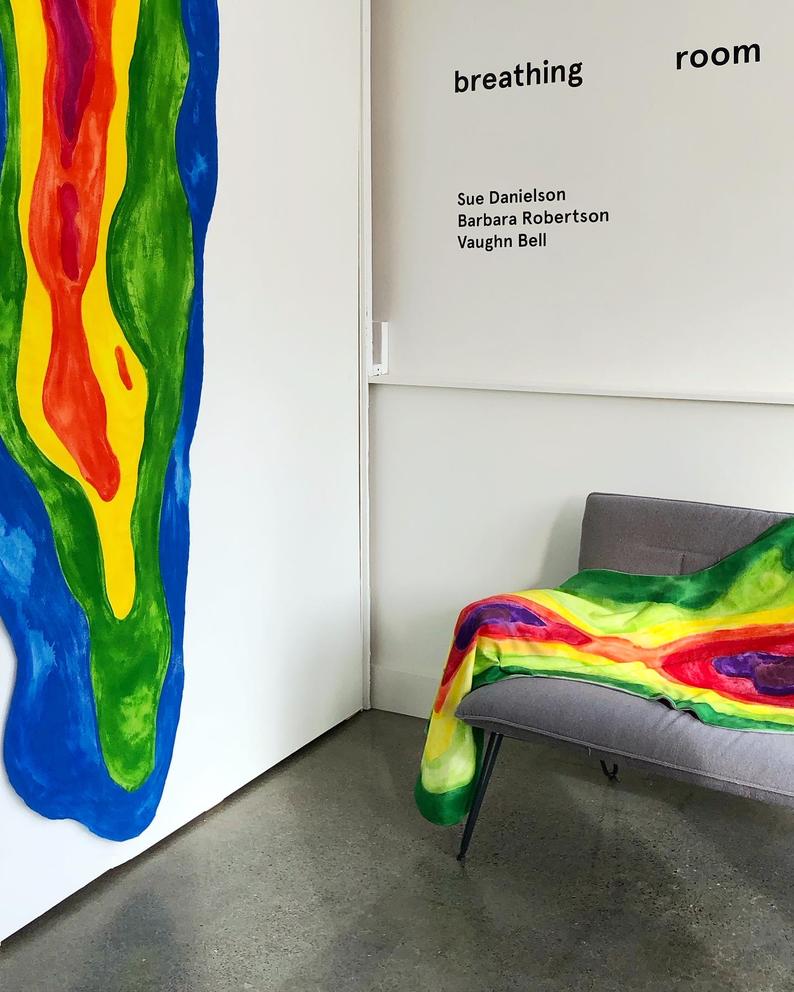 A hanging rainbow blanket and another rainbow blanket on a couch; a sign above that says "breathing room"