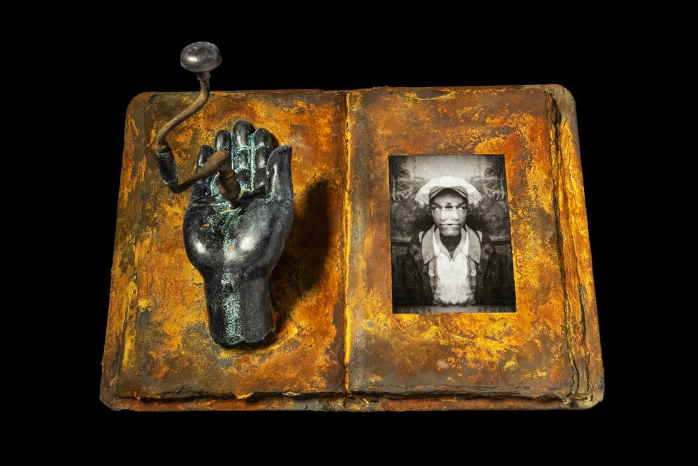 An open gold book has a sculpture of a hand sticking out on the left and a picture on the right