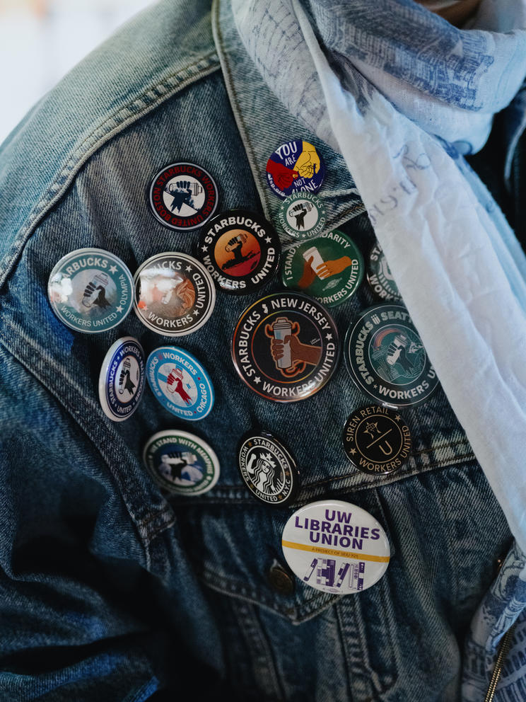 More than a dozen round Starbucks union and other labor pins cover the right shoulder of a demin jacket.