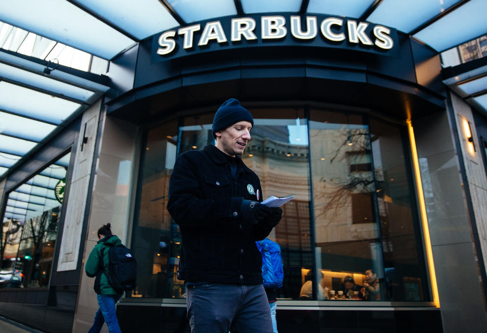A man in a black beanie hands out union fliers outside a Starbucks storefront.