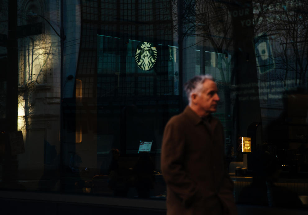 A man in dark clothes walks past a Starbucks storefront at night. 