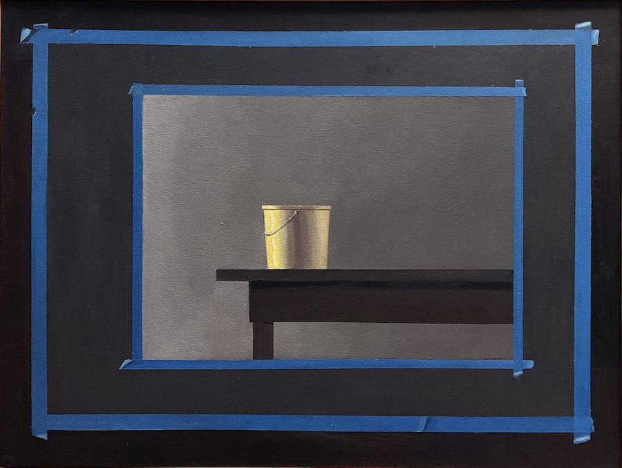 A yellow bucket sits on a table, framed twice with blue tape