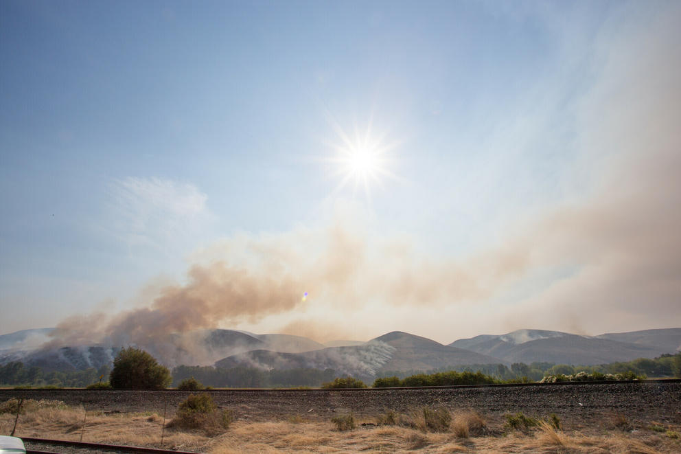 A sunny sky shows smoke rising from The Evans Canyon Fire. 