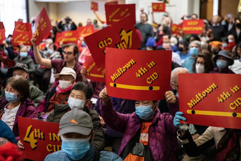 a group of mostly elderly asian residents in a meeting room, holding red signs. 
