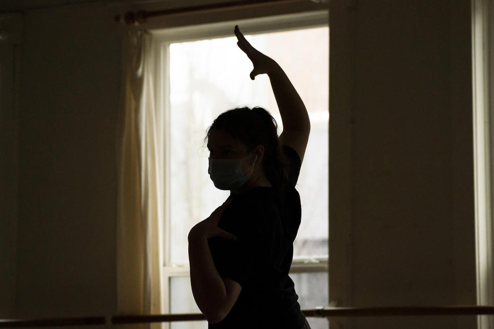 The silhouette of a dancer posing with an arm over her head in front of a window