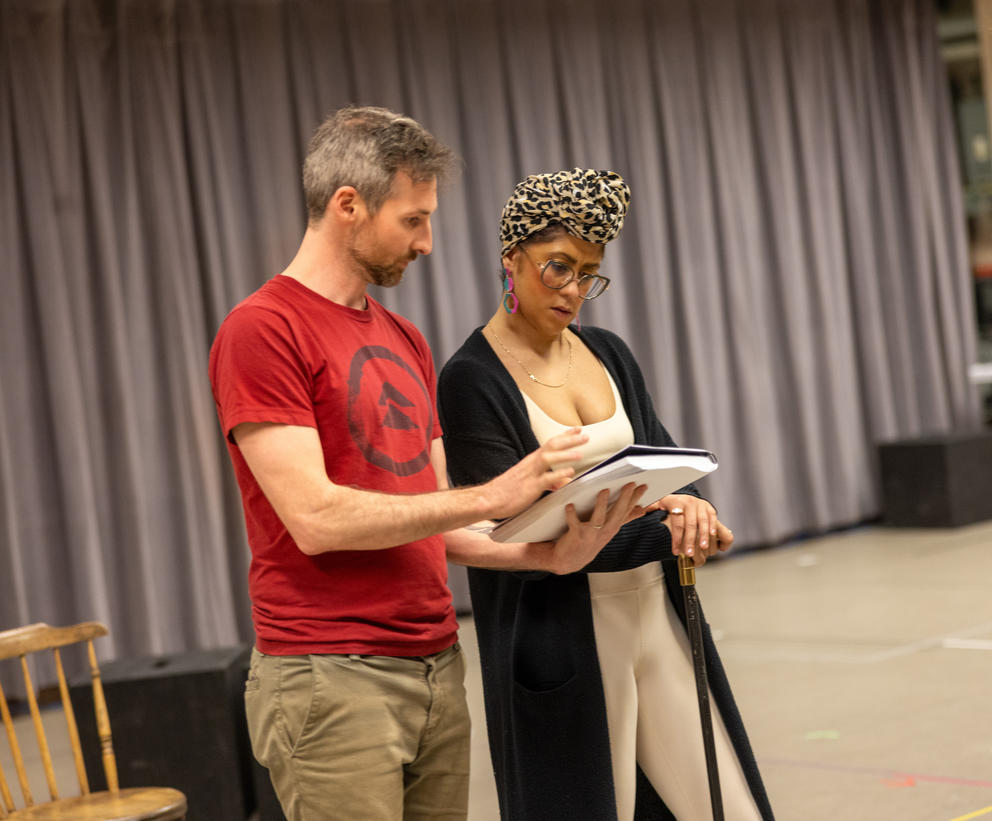 photo of a man and woman backstage, consulting a script during a rehearsal