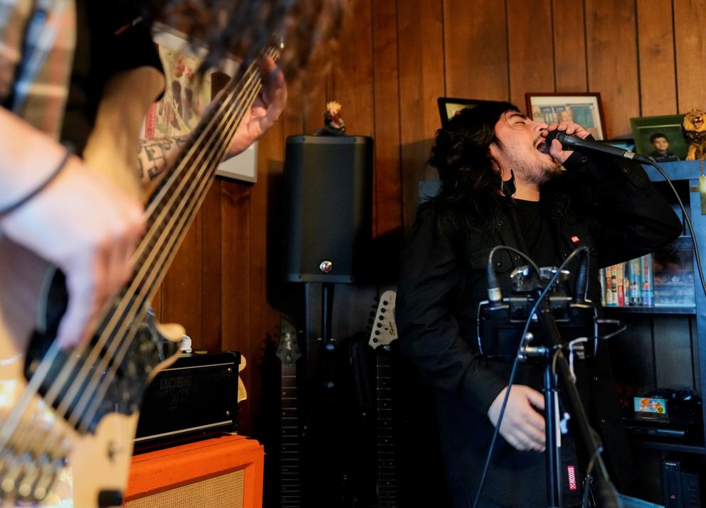 Camara sings into a microphone next to the guitarist of his band The Lion & The Sloth at his home.