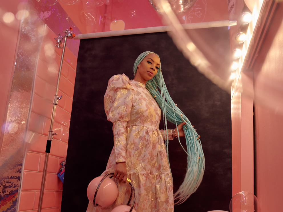 photo of a woman in a pink room wearing a pink dress with long turquoise braids
