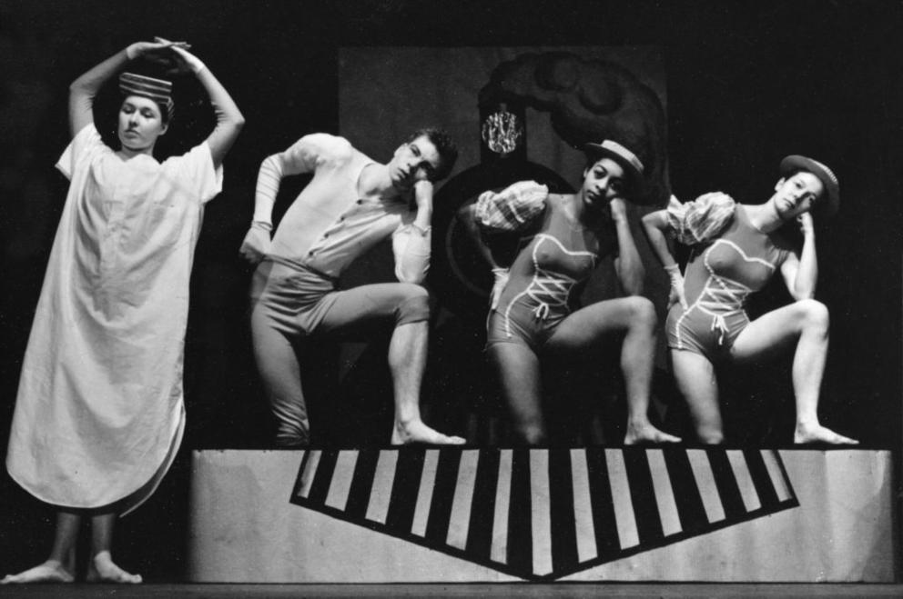 an archival photo of four dancers on stage in unusual positions facing forward, heads on hands, elbows on raised knees
